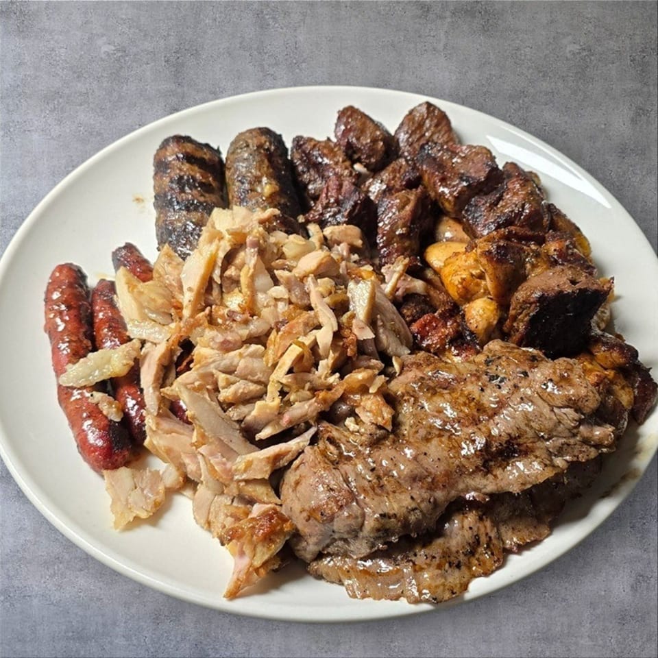 A white plate piled high with grilled meats, including sausages, shredded chicken, and steak.