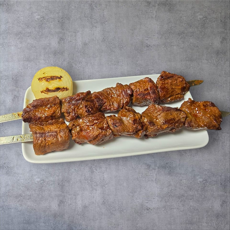 Two skewers of grilled beef cubes and a grilled onion half on a white rectangular plate.