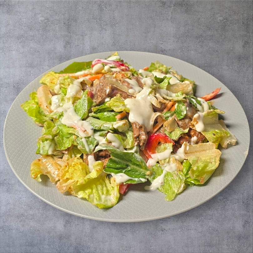 A fresh salad with lettuce, meat, red peppers, and a creamy white dressing on a gray plate.