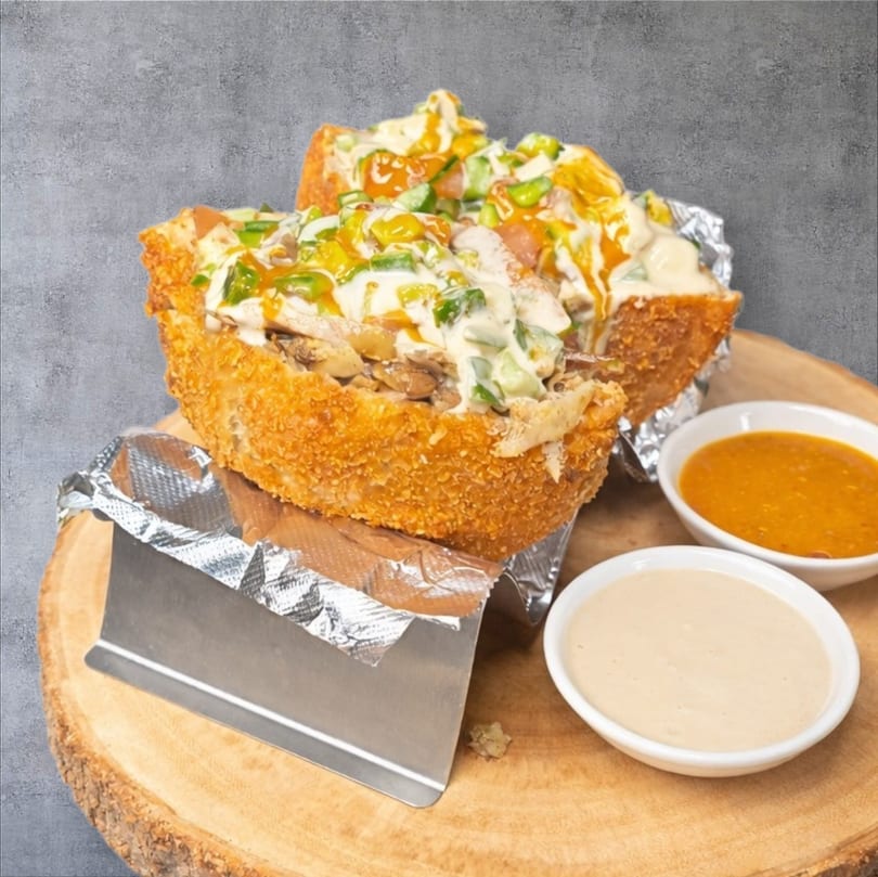Two crispy bread bowls filled with chicken, vegetables, and creamy sauces, served with dips.